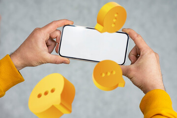 A close-up of a hand holding mockup smartphone with a blank screen, surrounded by floating yellow chat icons.