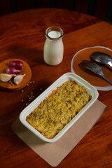 Cheesy baked rice casserole, served on rectangular bowl on a wooden table, in a cafe environment