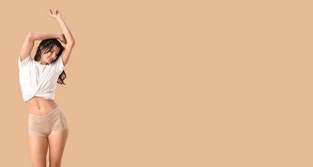 Pretty young woman in t-shirt and panties dancing on beige background with space for text