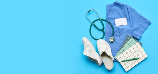 Doctor's uniform with notebooks, shoes and stethoscope on blue background with space for text