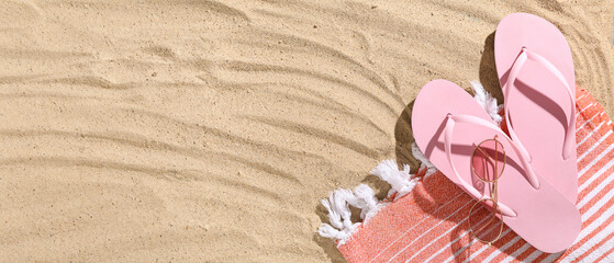 Pair of pink flip flops with sunglasses and blanket on sandy background