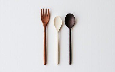 Three wooden utensils arranged on a neutral background. A fork, spoon and serving spoon in dark brown, off-white and light brown tones. Flatlay photography