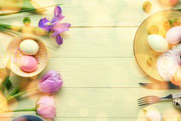 Frame made of different flowers and painted eggs for Easter celebration on yellow wooden background