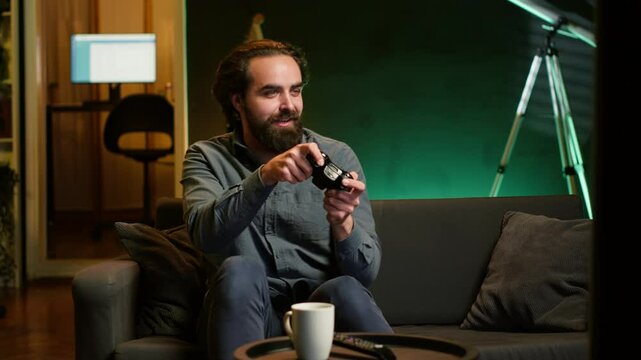 Happy man playing videogame in neon illuminated home, holding controller. Gamer excited to participate in online tournament, battling other players using professional joypad