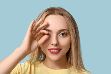 Young woman with vitamin A pill on blue background, closeup