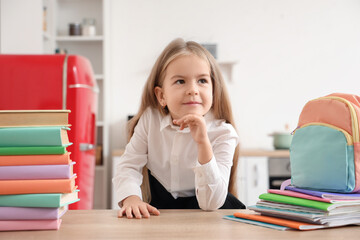 Cute little schoolgirl with backpack and books on table at home