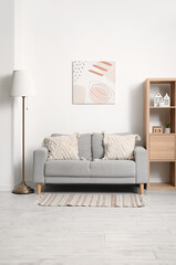 Interior of modern living room with comfortable sofa, lamp, picture and shelves