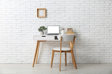 Stylish workplace with laptop and chair near white wall