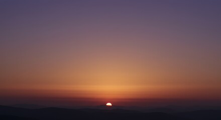 Fototapeta premium Serene Sunset Over the Mountains: A breathtaking view of the sun setting behind a distant mountain range, painting the sky with vibrant hues of orange, purple, and deep violet.