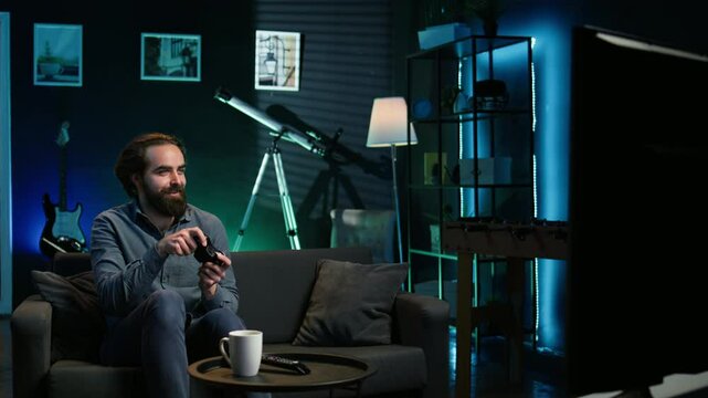 Happy man playing videogame in neon illuminated home, holding controller. Gamer excited to participate in online tournament, battling other players using professional joypad