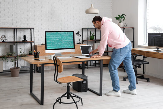 Portrait of male programmer working with laptop and computer in modern office