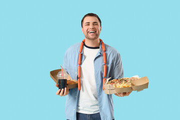 Young man with unhealthy food and soda on blue background. Overeating concept