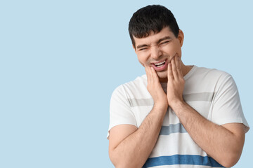 Young man suffering from toothache on blue background, closeup