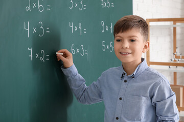 Cute boy writing on chalkboard during lesson in classroom