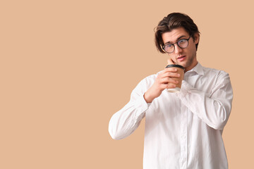 Weary young businessman with coffee cup on beige background