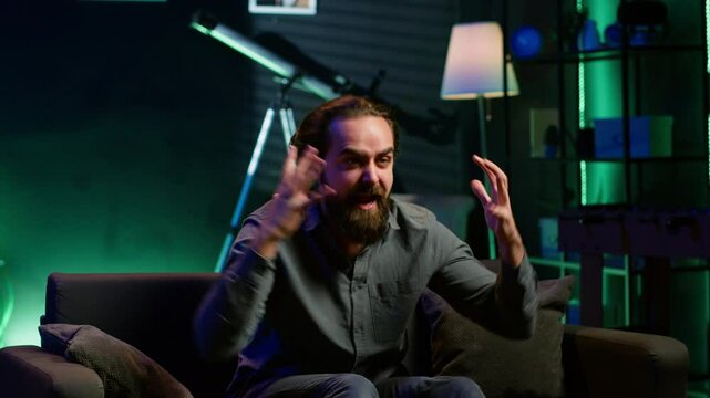 Irked supporter raging while watching sports broadcast, berating team after mistake. Angry man throwing pillow at TV screen while looking at football, scolding player for missing chance, camera A