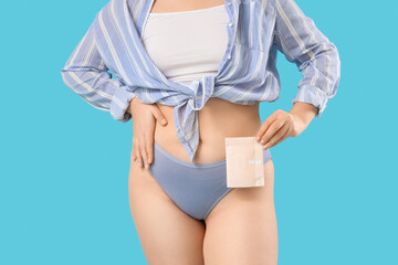 Young woman in period panties holding pad on blue background