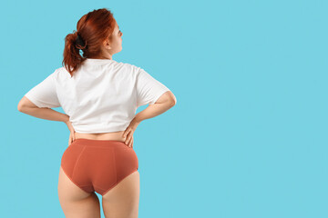 Young woman in period panties on blue background, back view