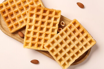 Wooden board with tasty Belgian waffles and nuts on beige background