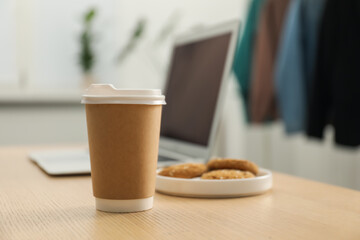 Paper cup, plate with cookies and laptop on wooden table indoors, closeup. Mockup for design