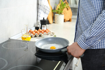 Man cooking egg in frying pan on cooktop indoors, closeup