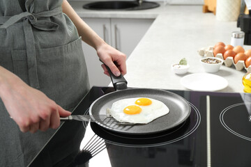 Woman taking fried eggs from frying pan in kitchen, closeup