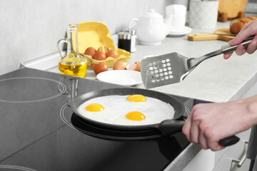 Woman cooking eggs in frying pan on cooktop indoors, closeup