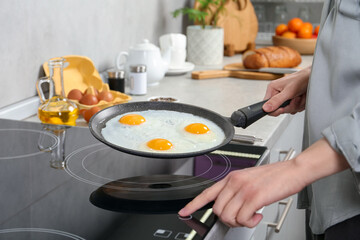 Woman cooking eggs in frying pan on cooktop indoors, closeup