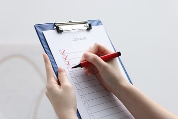 Woman filling Checklist on blurred background, closeup