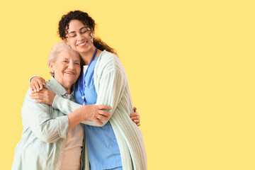 Young African-American female medical worker with elderly woman against yellow background