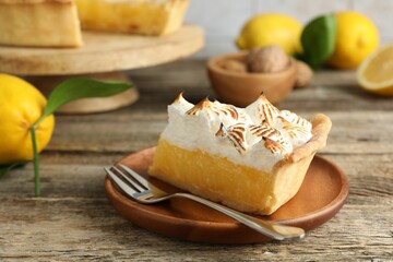 Piece of delicious pie with browned meringue and fork on wooden table, closeup