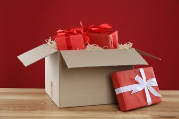 Parcel with gift boxes on wooden table against red background