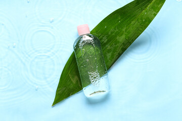 Bottle of micellar water and green leaf on wet blue background