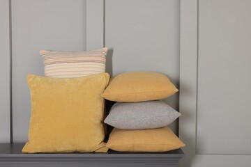 Soft decorative pillows on chest of drawers near grey wall
