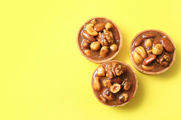 Tasty tarts with nuts and caramel on yellow background