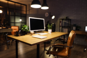 Blurred view of workplace with computer, plants and glowing lamps in dark office