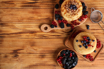 Boards of sweet pancakes with different fresh berries and nuts on wooden background
