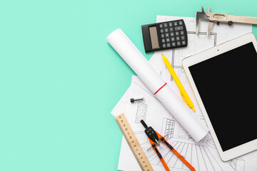 Architect's supplies with house plans and tablet computer on green background