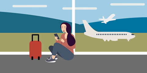 Female passenger of Asian descent sitting on the floor in the airport using smartphone waiting for the flight