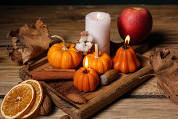 Burning candles with pumpkins, apple, cinnamon, dried orange, acorns and autumn leaves on wooden table