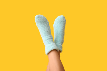 Legs of young woman in warm blue socks on yellow background