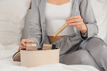 Young beautiful woman with cosmetic box on bed in room