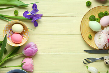 Frame made of different flowers and painted eggs for Easter celebration on yellow wooden background