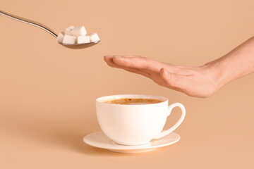 Female hand with cup of coffee rejecting sugar on beige background