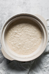Overhead view of focaccia dough on a white marble countertop, top view of homemade focaccia bread dough in a claypot, process of making focaccia