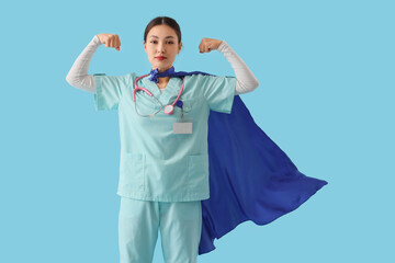 Female Asian doctor with superhero cape showing muscles on blue background. International Nurses Day © Pixel-Shot