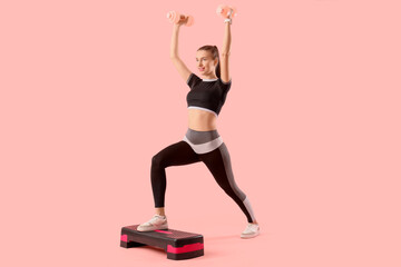 Sporty young woman training with dumbbells and stepper on pink background