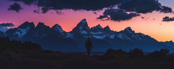 Fototapeta premium A person walks towards a mountain range at sunset or sunrise