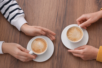 Coffee break. Women with cups of hot drinks at wooden table, top view