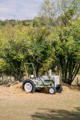 Fototapeta premium Small gray tractor stands on hay near green trees
